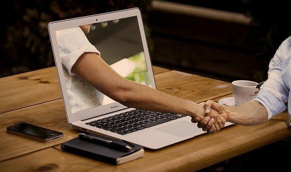 Photo d'un ordinateur portable sur le bureau, montrant un bras tendu vers l'extérieur de l'écran de l'ordinateur portable pour serrer la main d'un autre bras posé sur le bureau.