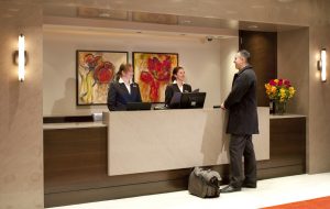 Two female front desk employees speak to a male guest in a hotel lobby.