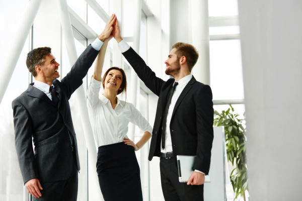 Three office workers raise their hands in a three-way high five.