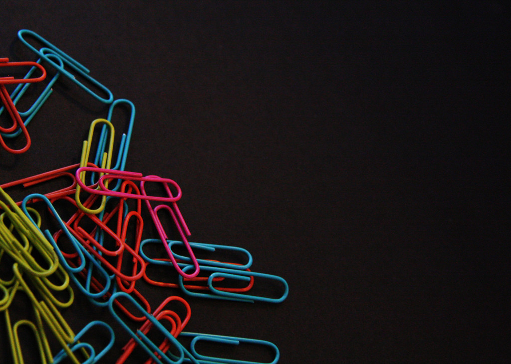 Photo of a handful of brightly colored paperclips against a black background.