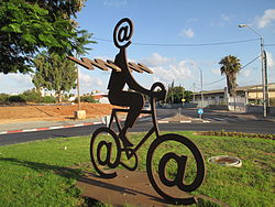 Sculpture of a man with an "@" symbol head and wings, riding on a bike with @ wheels.
