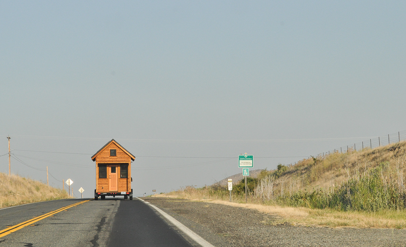 Photo of a tiny house being pulled on a trailer on a road.