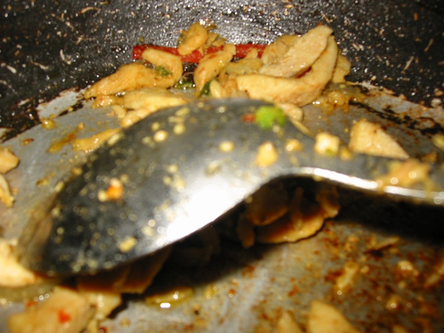 a close up of a spoon in a pan full of sautéed pieces of chicken and seasonings