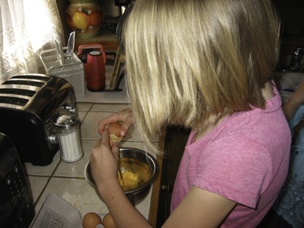 a young person cracking an egg into a bowl in a kitchen