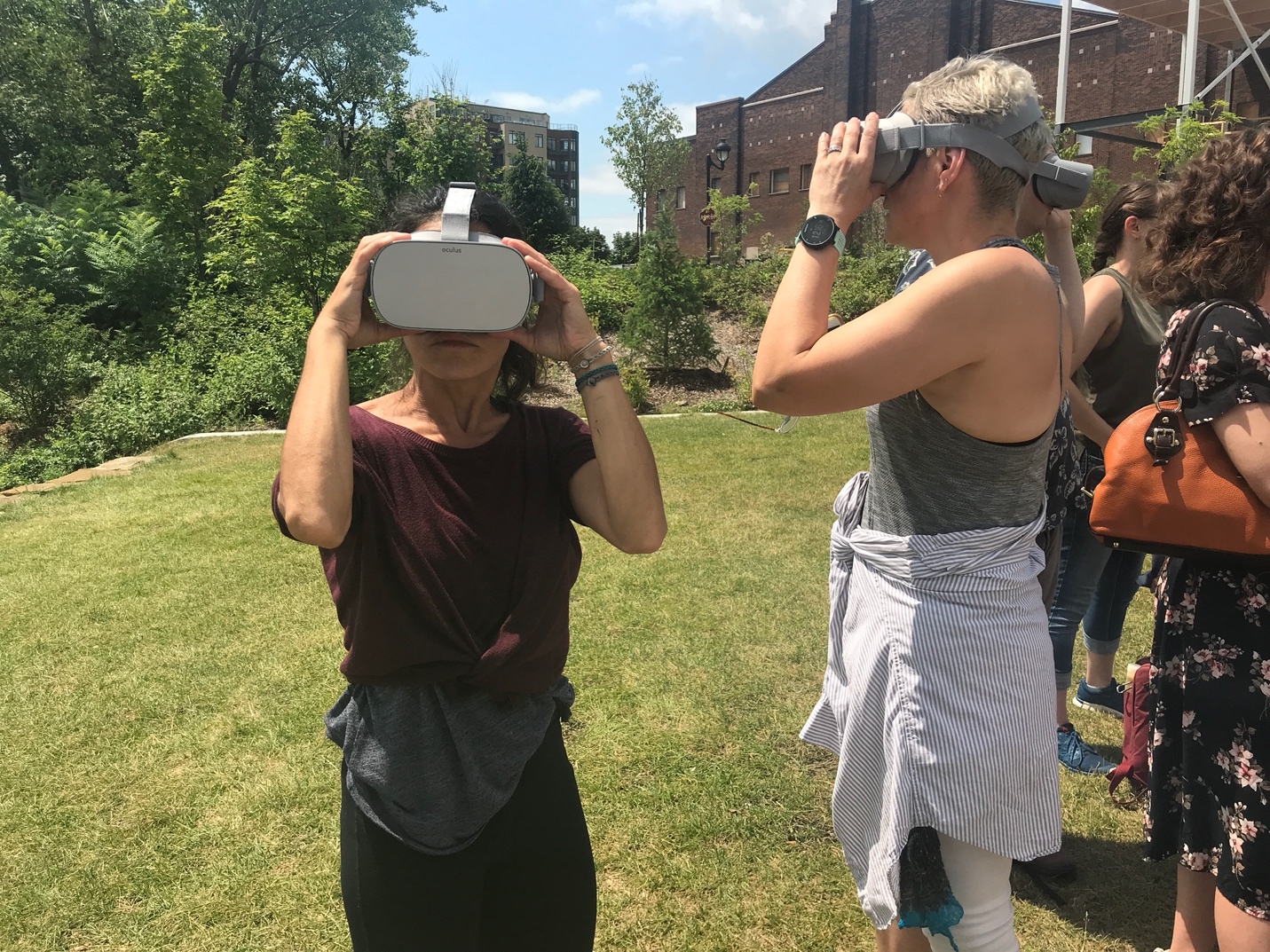 two people on a grassy slope looking through virtual reality visors