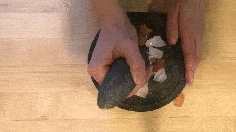 animated GIF of two hands crushing egg shells in a mortar