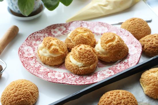 Photo of filled cream puffs on a plate with unfilled choux pastry surrounding the plate
