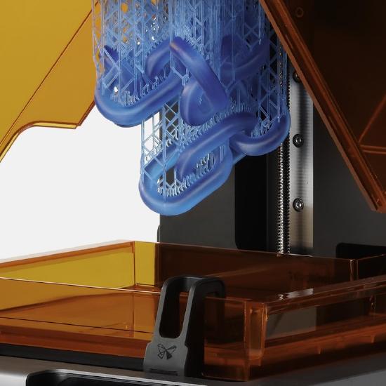 A group of oval chain links in the print bed area of the 3D printer. Connected to the chain links is an extensive lattice network of much thinner structures.
