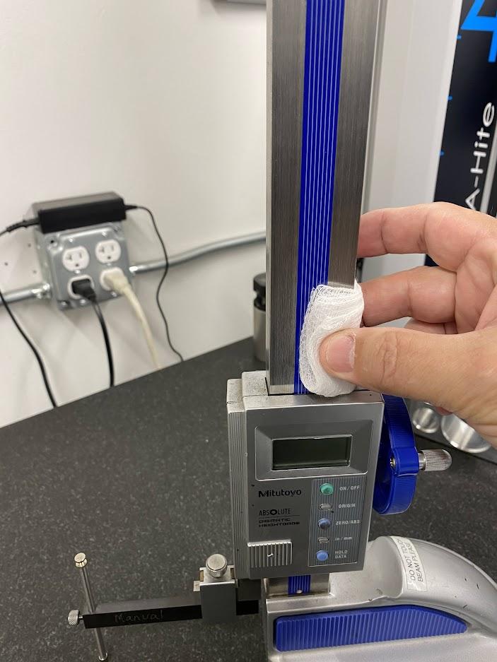 A hand is wiping white gauze on the beam of a height gage.