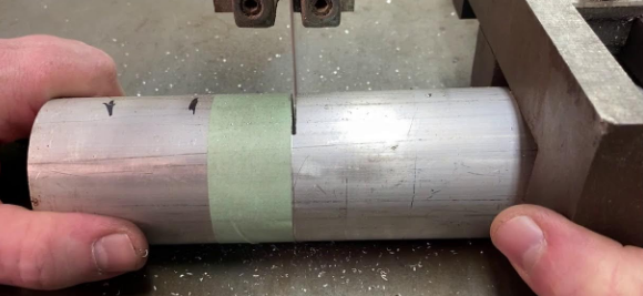 A square block is clamped onto a round part to keep it from spinning when cut.