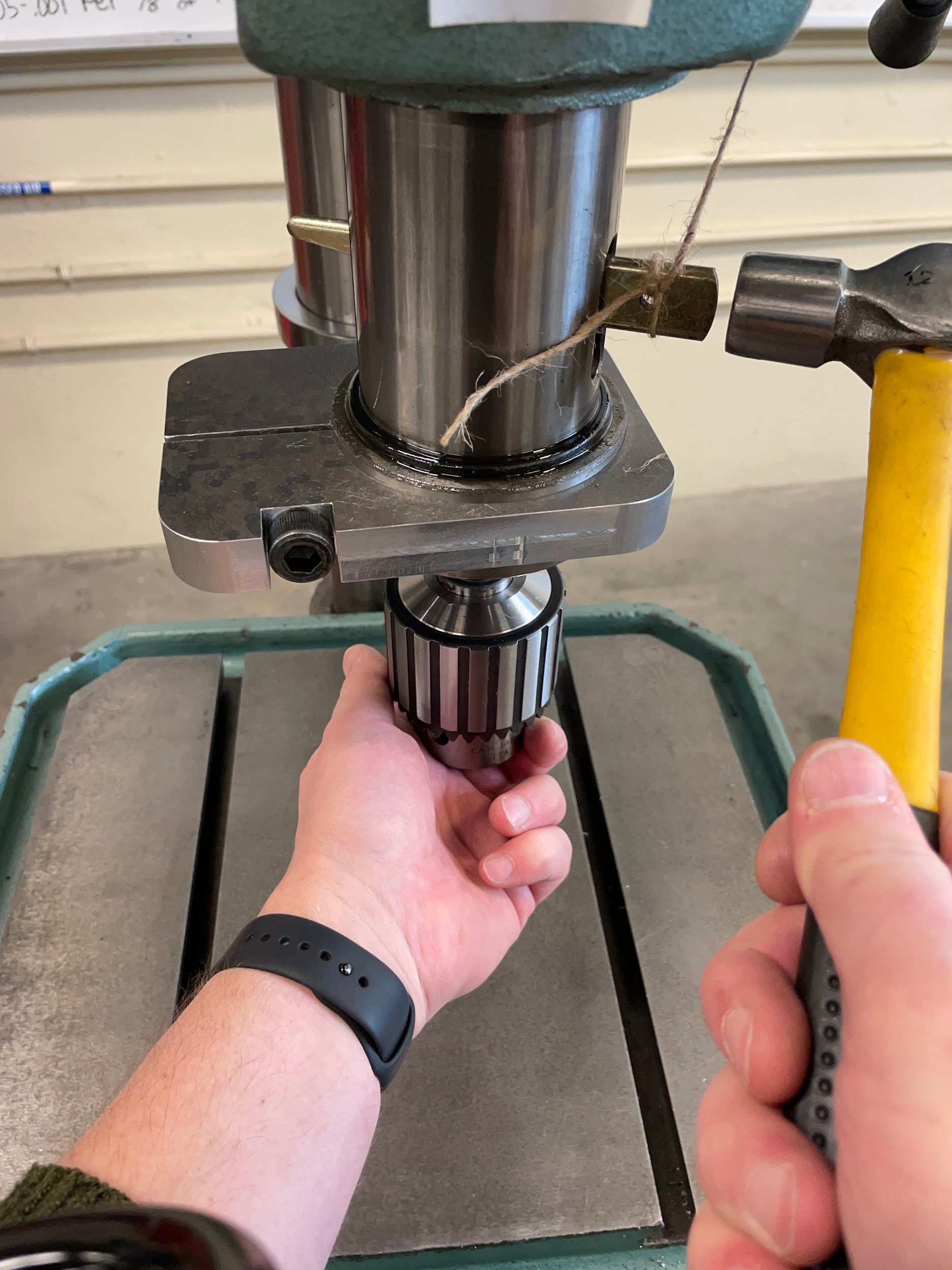 Tapping on the end of a drill drift with a hammer to remove a drill chuck from the spindle of a drill press.