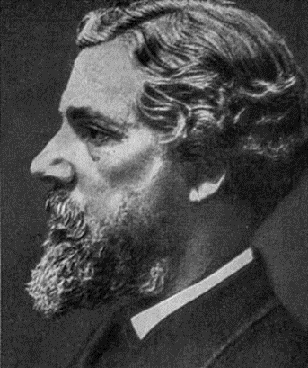Profile portrait of a man with a beard and wavy hair, wearing a suit, set against a dark background.