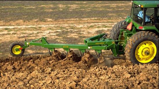 A green tractor plowing a field, breaking up the soil with its attached plow.