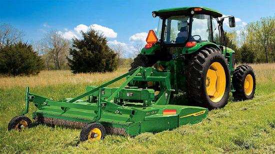 A green tractor with a yellow wheel parked in a grassy field, equipped with a mowing attachment for cutting grass.