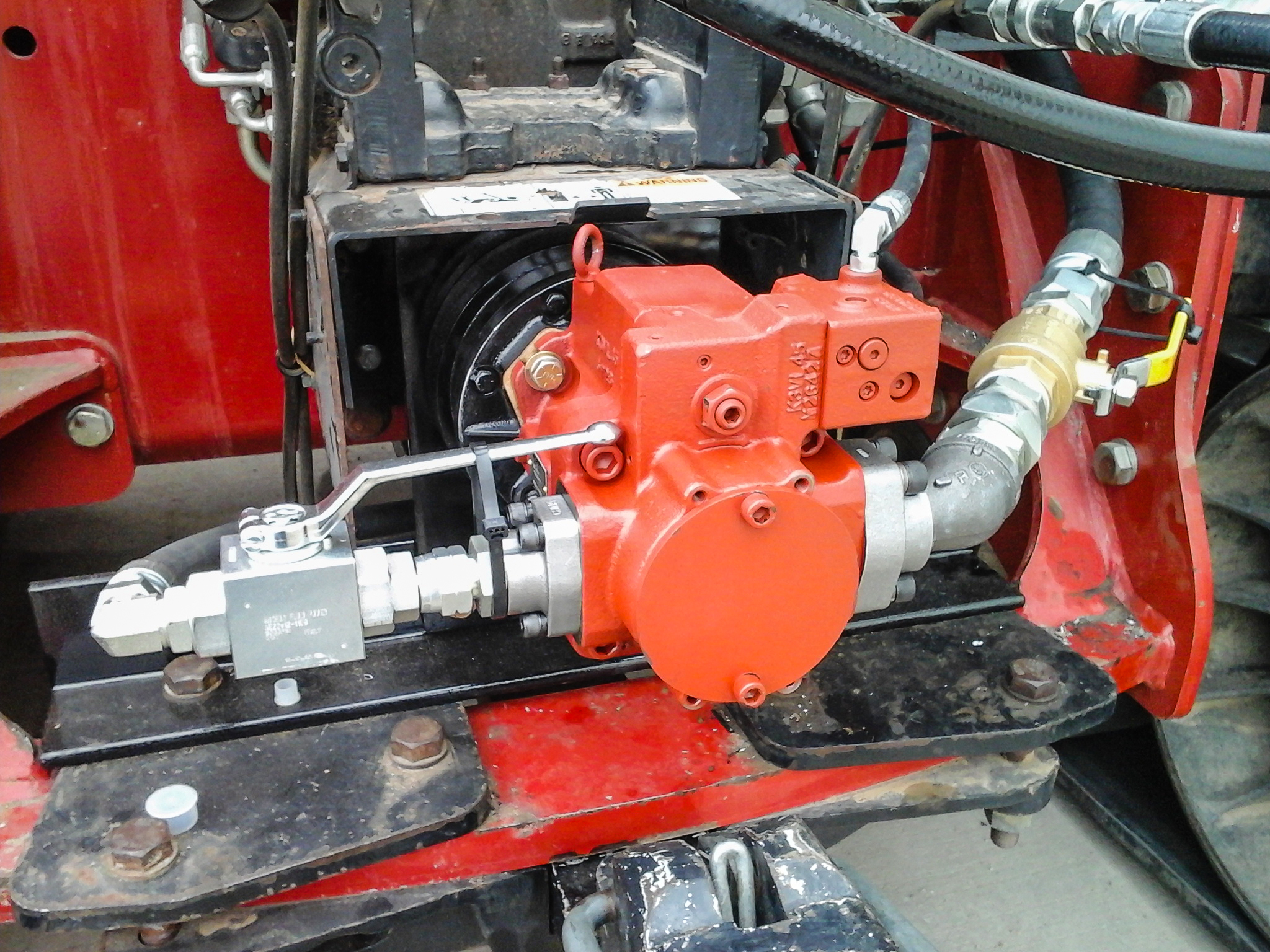 Close-up of a red hydraulic pump mounted on machinery, with various hoses and fittings visible.