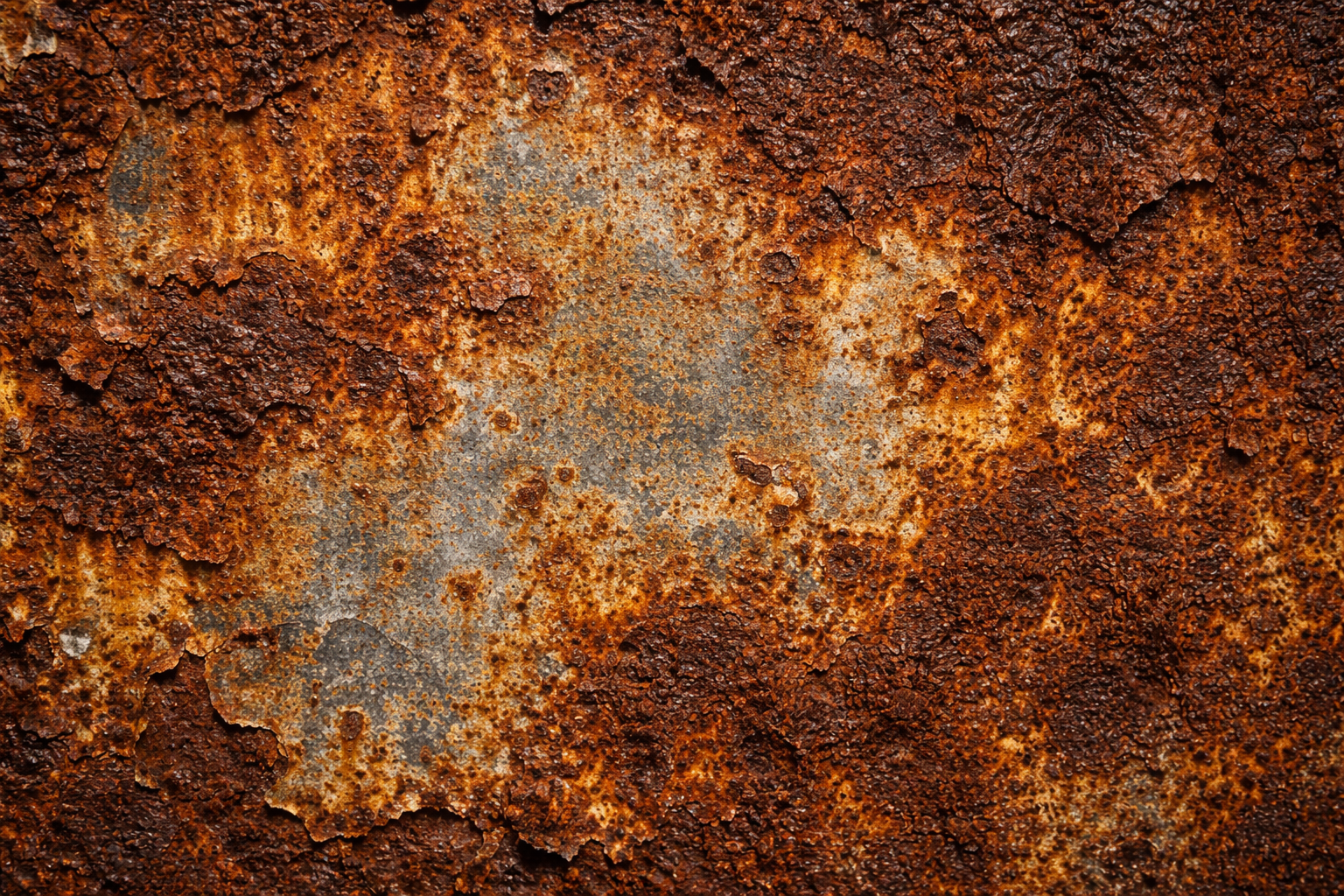 Close-up of a rusty metal surface with varying shades of orange and brown, featuring flaking and pitting textures.