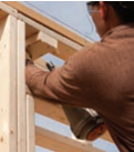 man using nail gun on frame of building