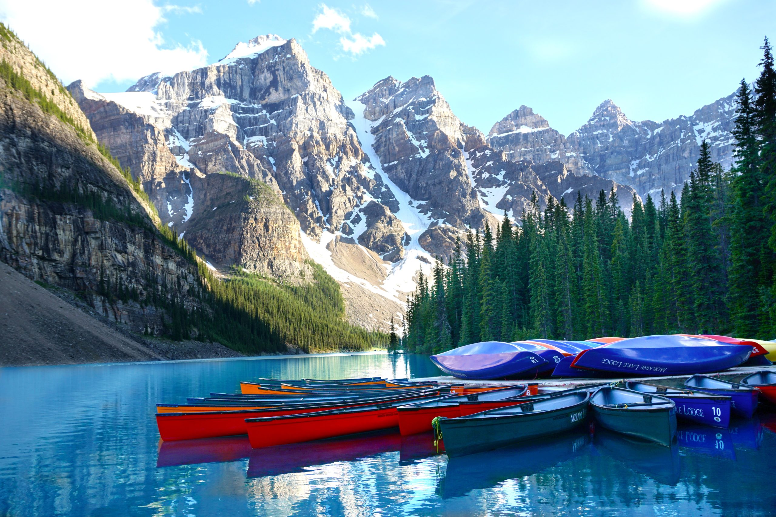 Canoas flotando en un lago azul prístino con imponentes montañas y árboles al fondo.