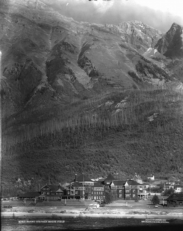 Un hotel junto a un ferrocarril al pie de una montaña.