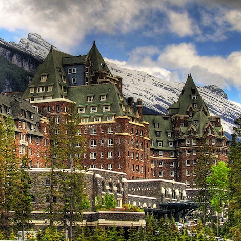 Un gran hotel con paredes de ladrillo y muchos techos a dos aguas frente a una montaña nevada.
