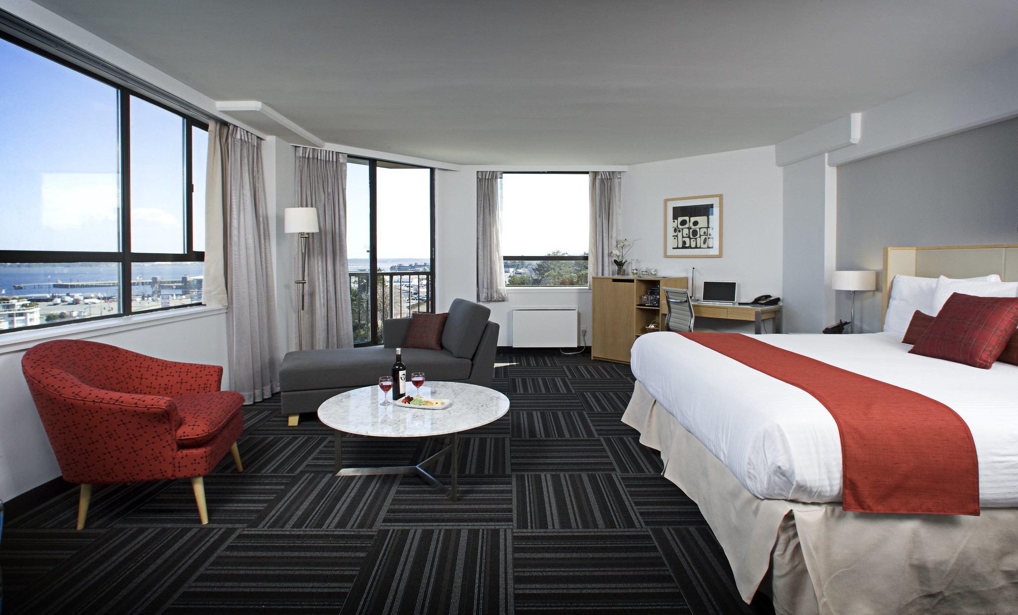 Una habitación de hotel con una cama grande, un sillón, una tumbona y un gran ventanal con vista al océano.