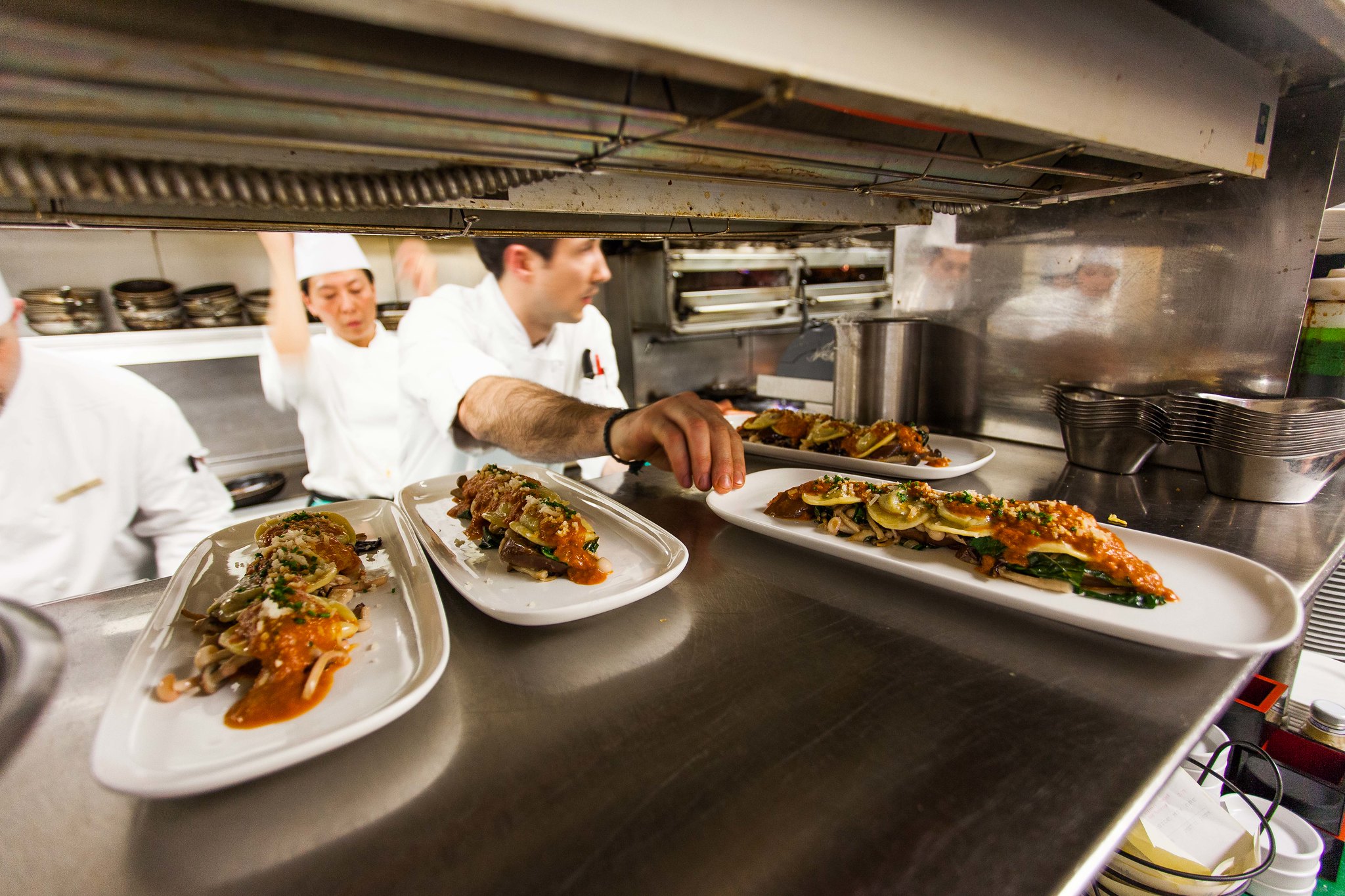 Un chef pone platos de comida gourmet en el paso a través de una cocina ocupada.