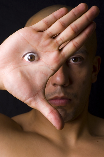 Un hombre sosteniendo una mano frente a donde debería estar un ojo, pero el ojo aparece en su mano.