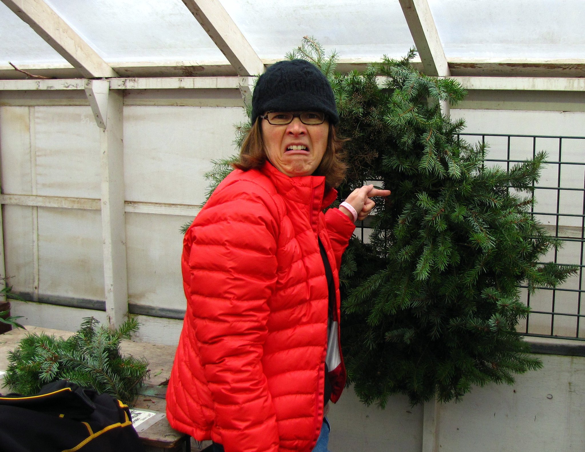 A woman makes a disgusted face and points to a messy pine wreath.