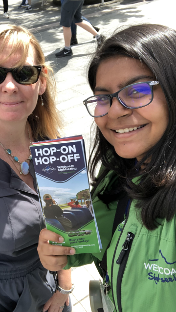 Two women pose with a brochure for a hop-on, hop-off bus tour.
