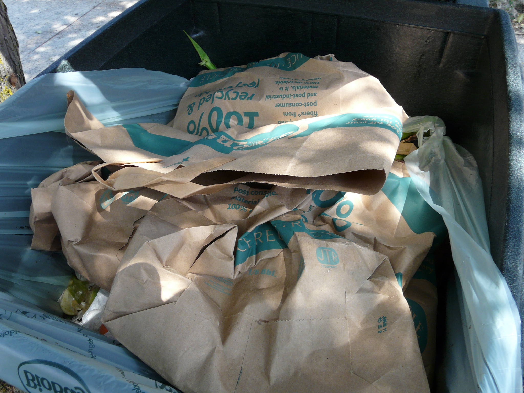 Varias bolsas marrones para desechos de alimentos en una papelera de compost con forro de plástico.