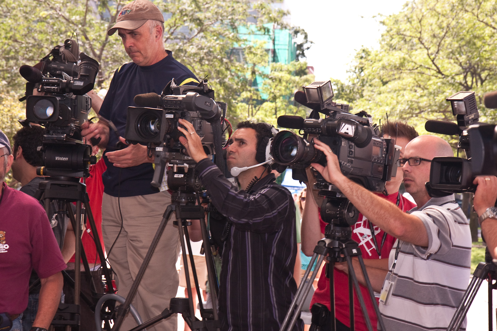 Several people operate four video cameras on tripods close together. One wears a headset.