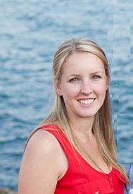 A headshot of a young woman in a red top by the ocean.