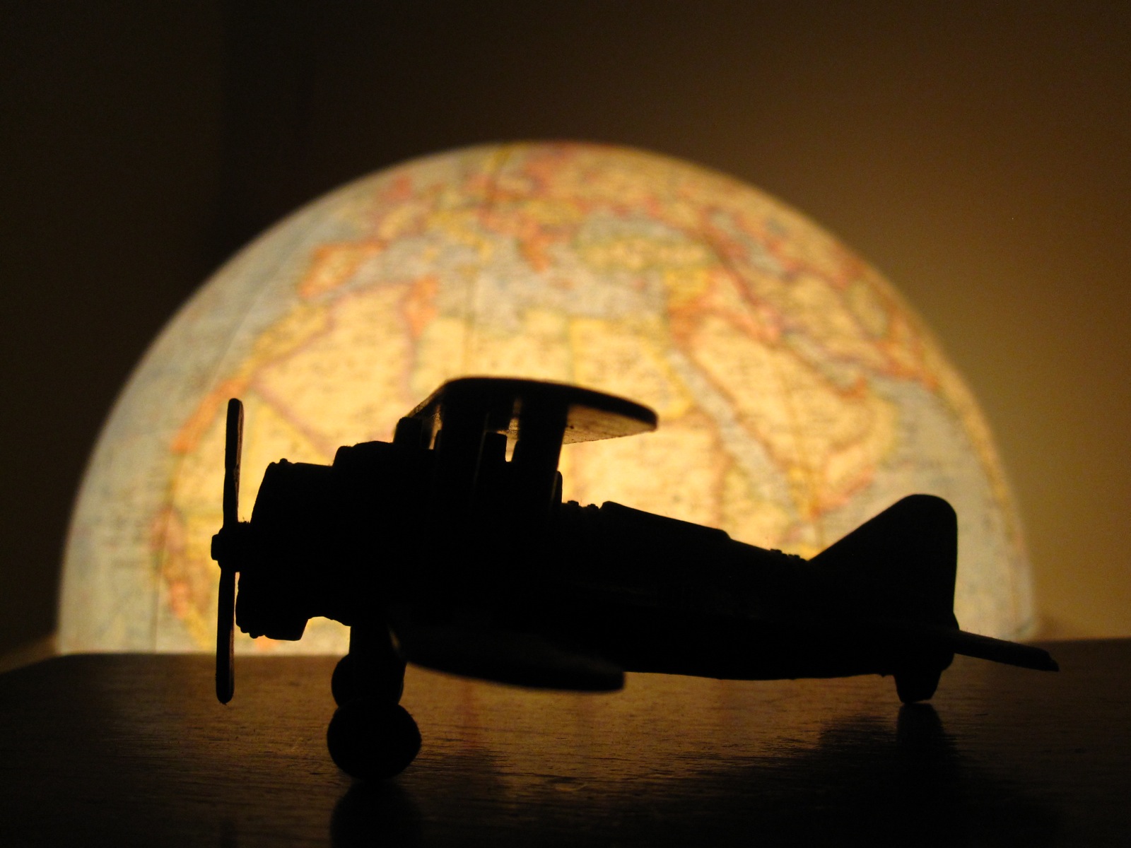 A toy airplane sits on a table in the dark. Behind it is a glowing globe.