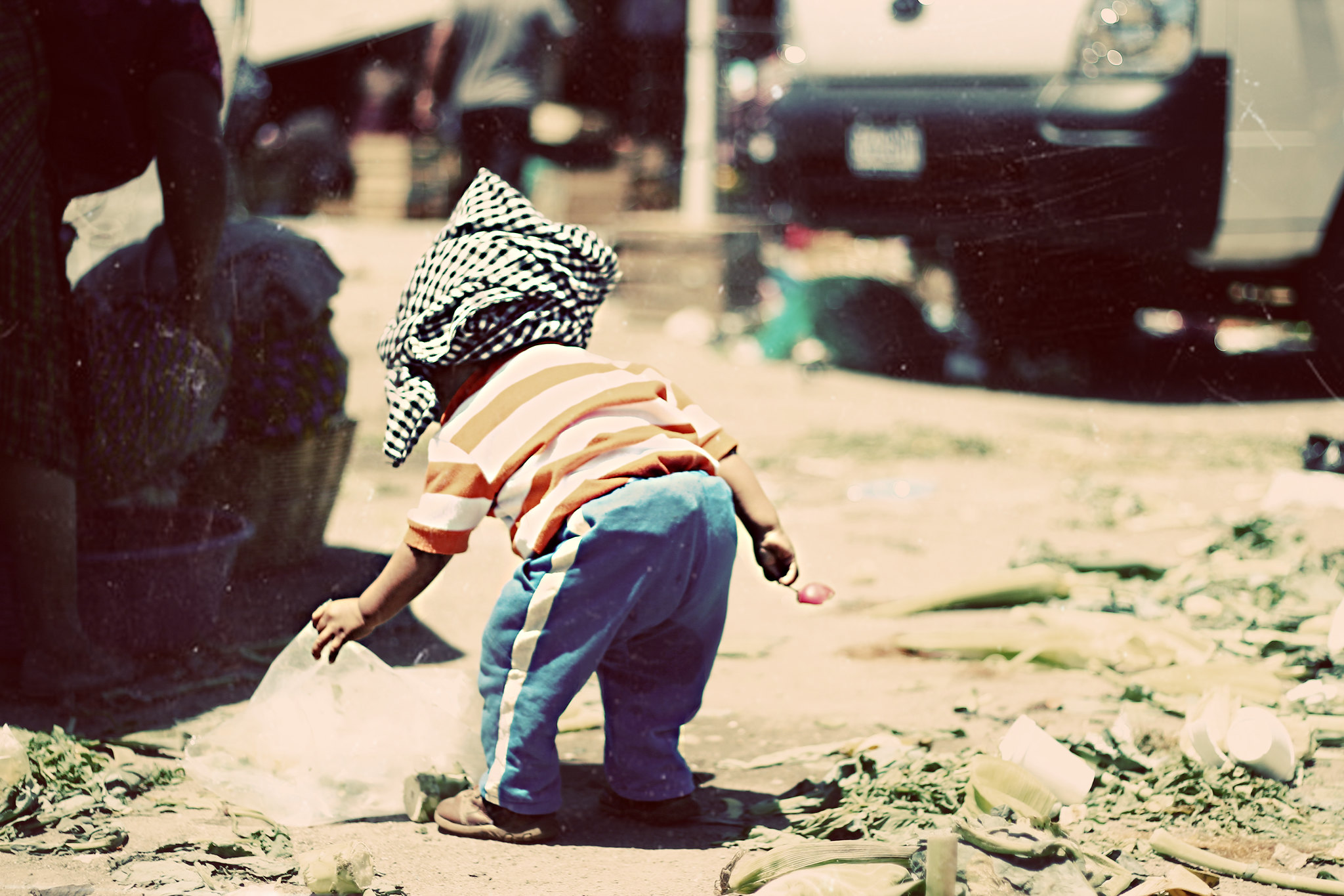 Un niño pequeño con tela envuelta alrededor de la cabeza juega con escombros en la calle.