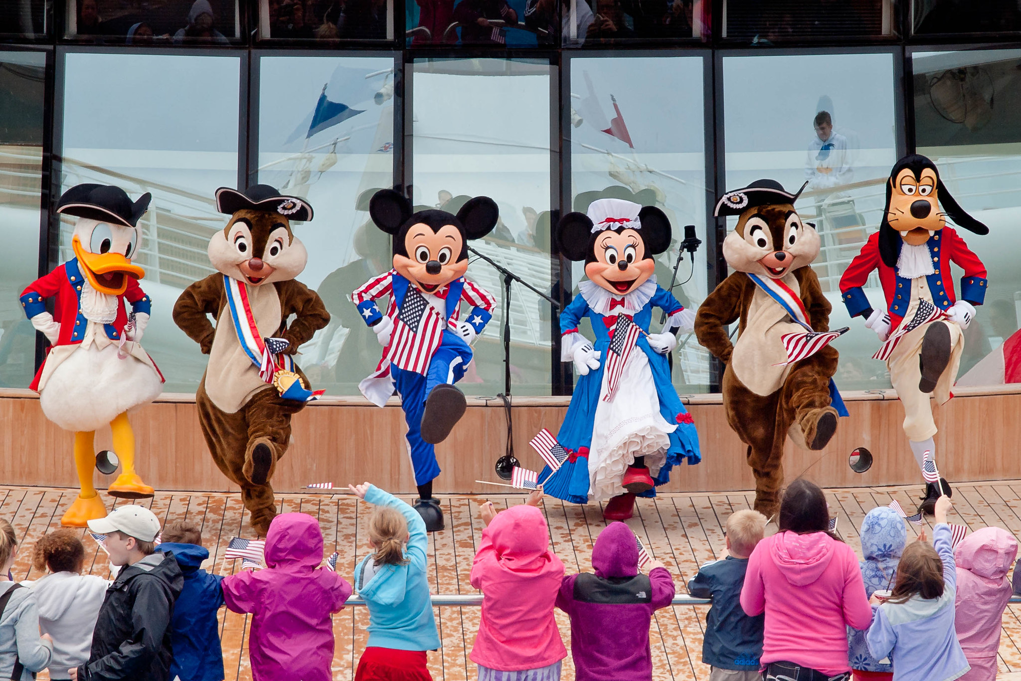 Personas vestidas con trajes clásicos de personajes de Disney actúan para una multitud de niños.