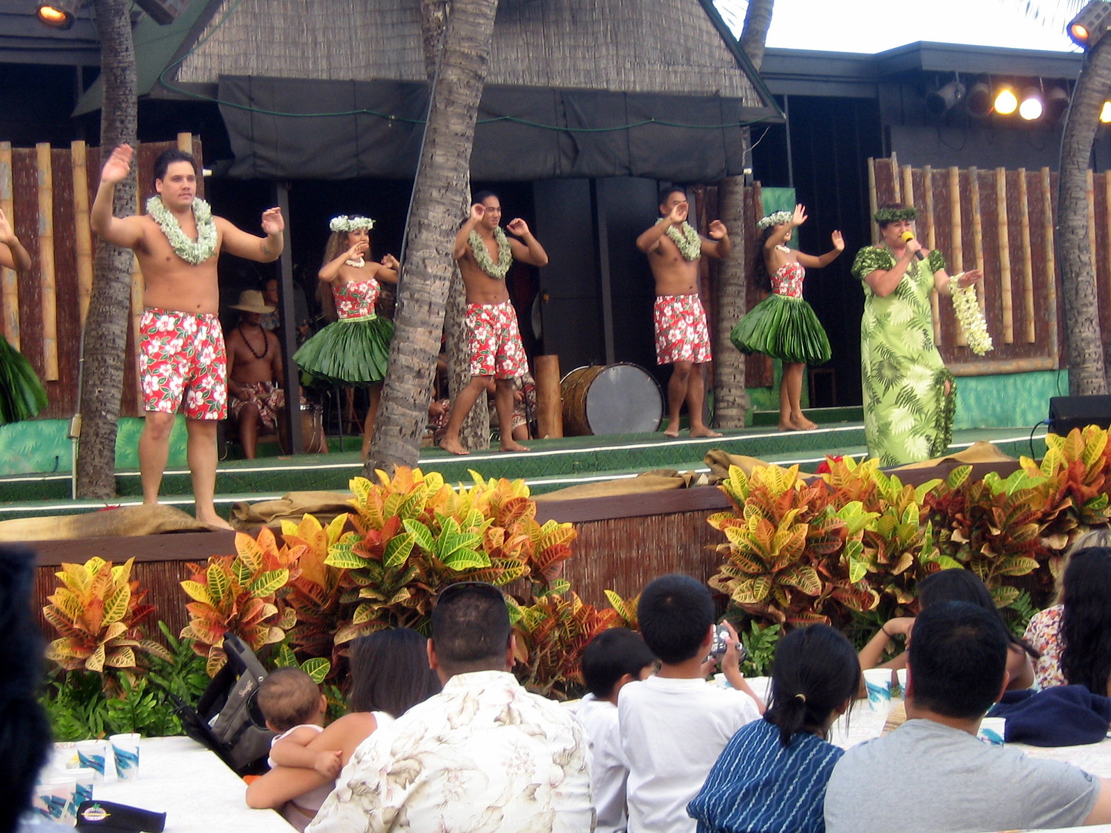 Bailarines con faldas de hierba, pantalones cortos de tabla y leis actúan en un escenario.