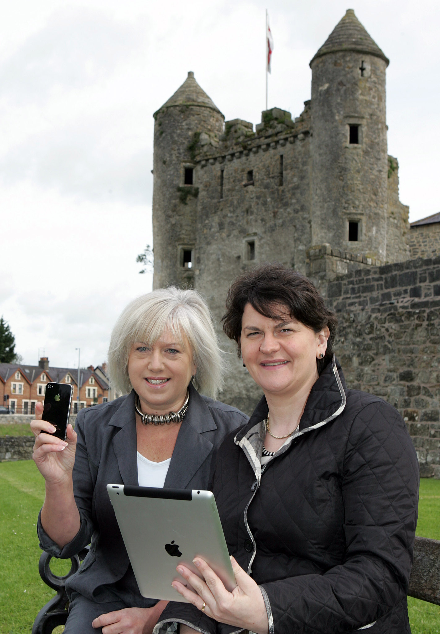Two women sitting in front of an old castle. One holds an iPhone, the other an iPad.